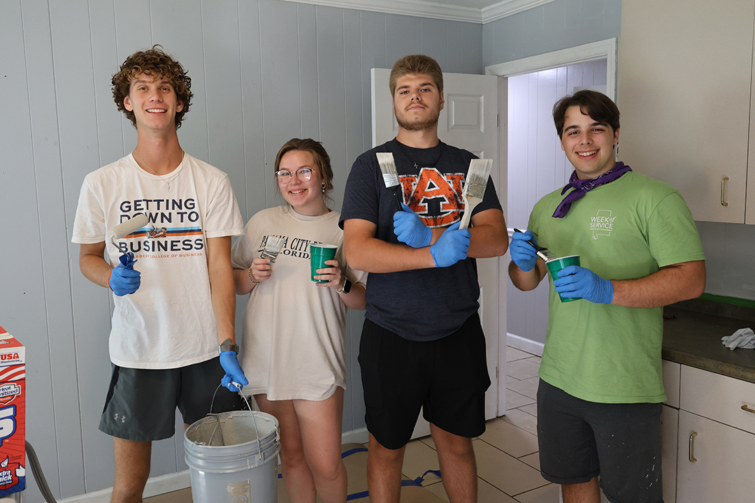 four students standing for a group photo with paintbrushes